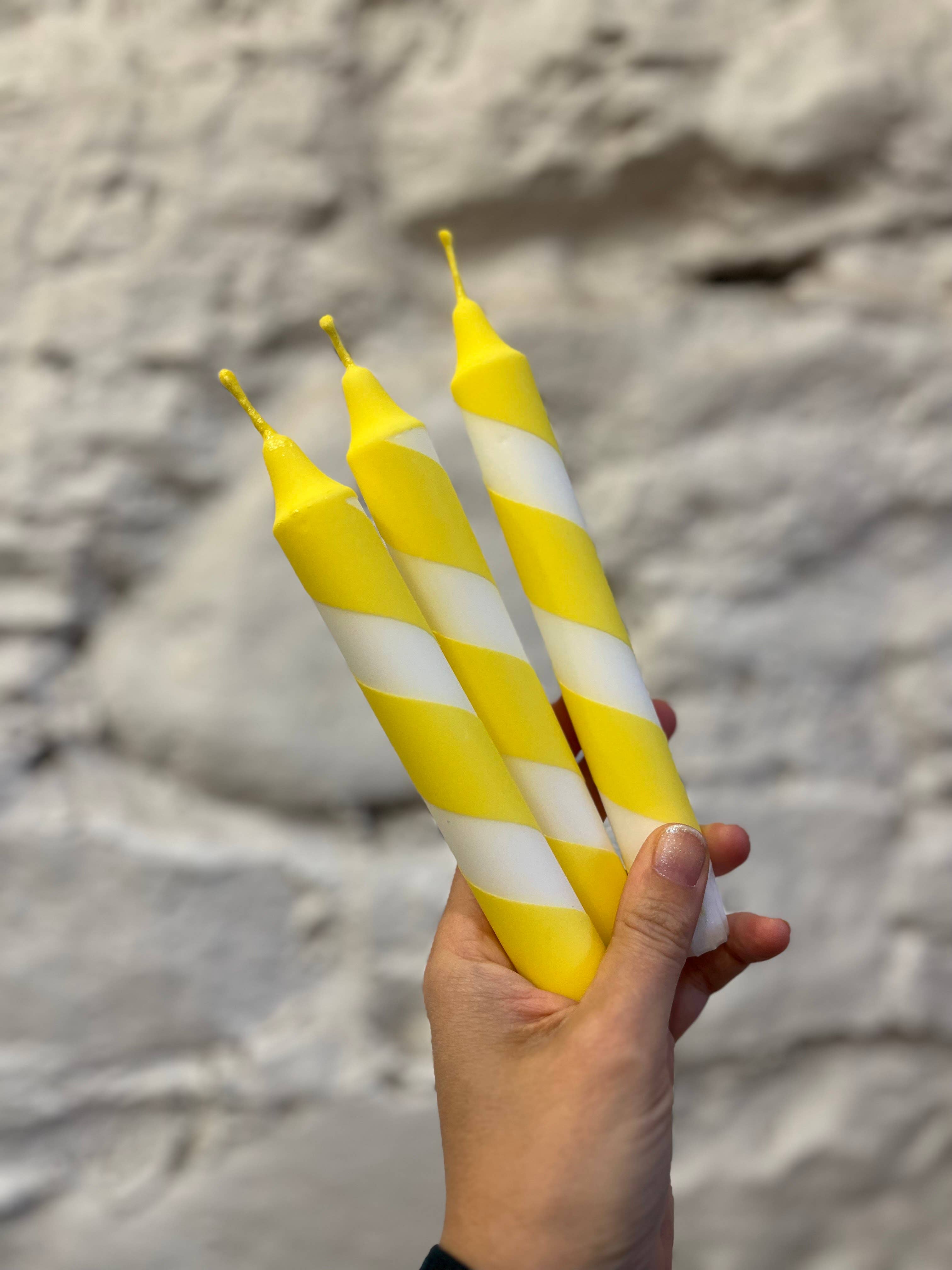 Hand holding yellow and white striped candles against a stone wall background