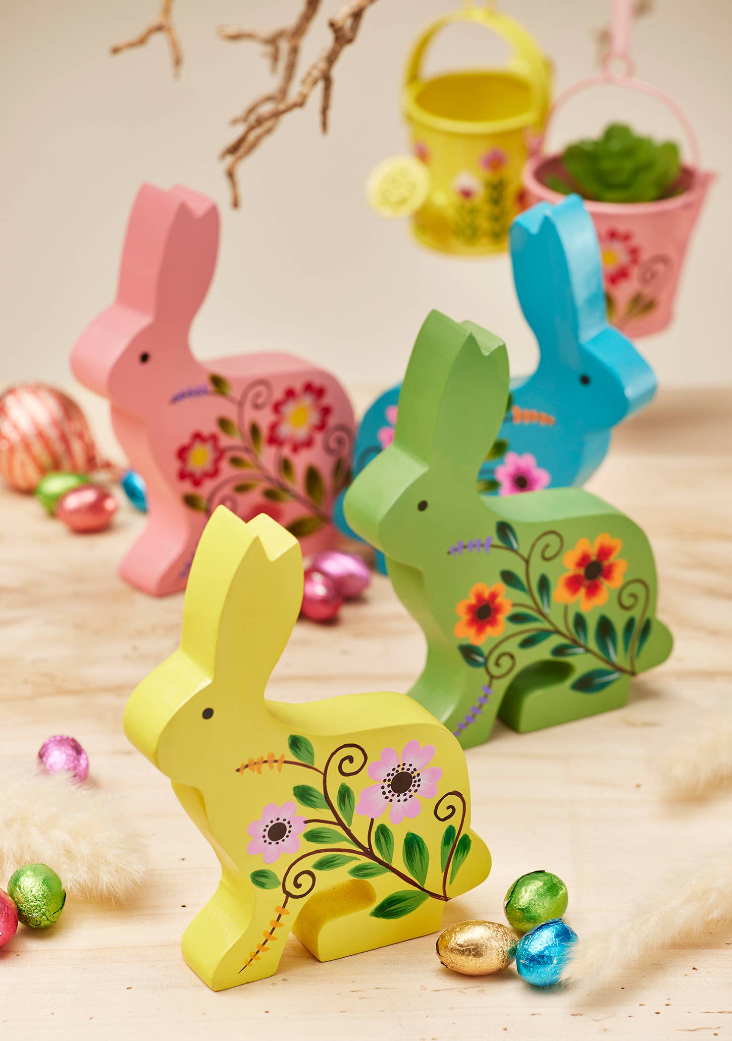 Colorful wooden Easter bunnies with floral designs on a wooden surface with Easter eggs.