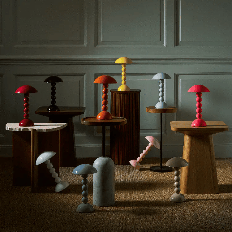 Collection of colorful table lamps on wooden stands against a paneled wall.