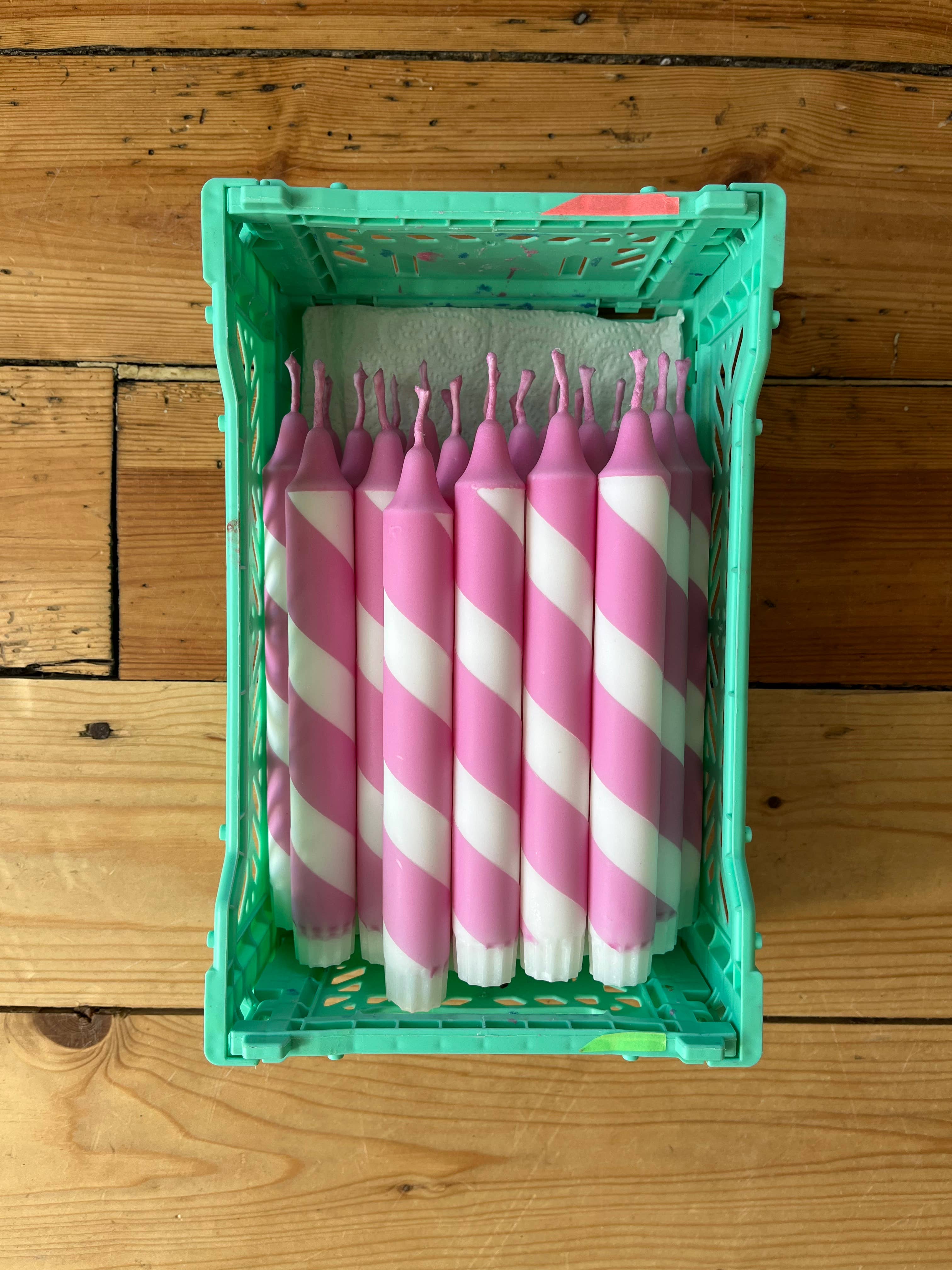 Pink and white striped candles in a green crate on a wooden surface
