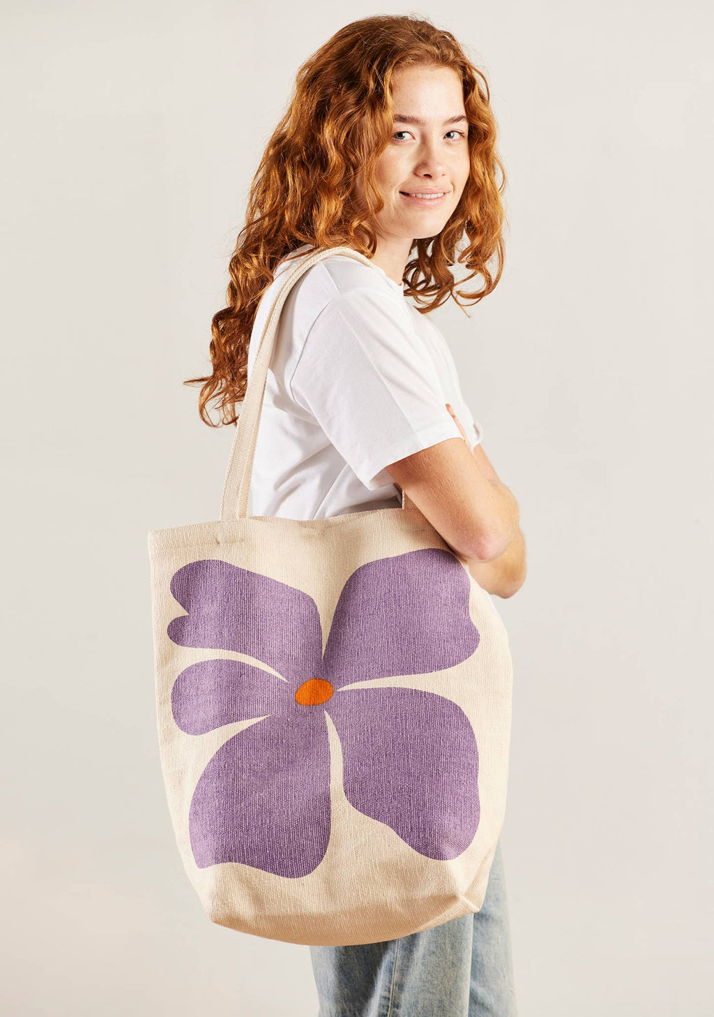Person holding a tote bag with a purple flower design on a plain background