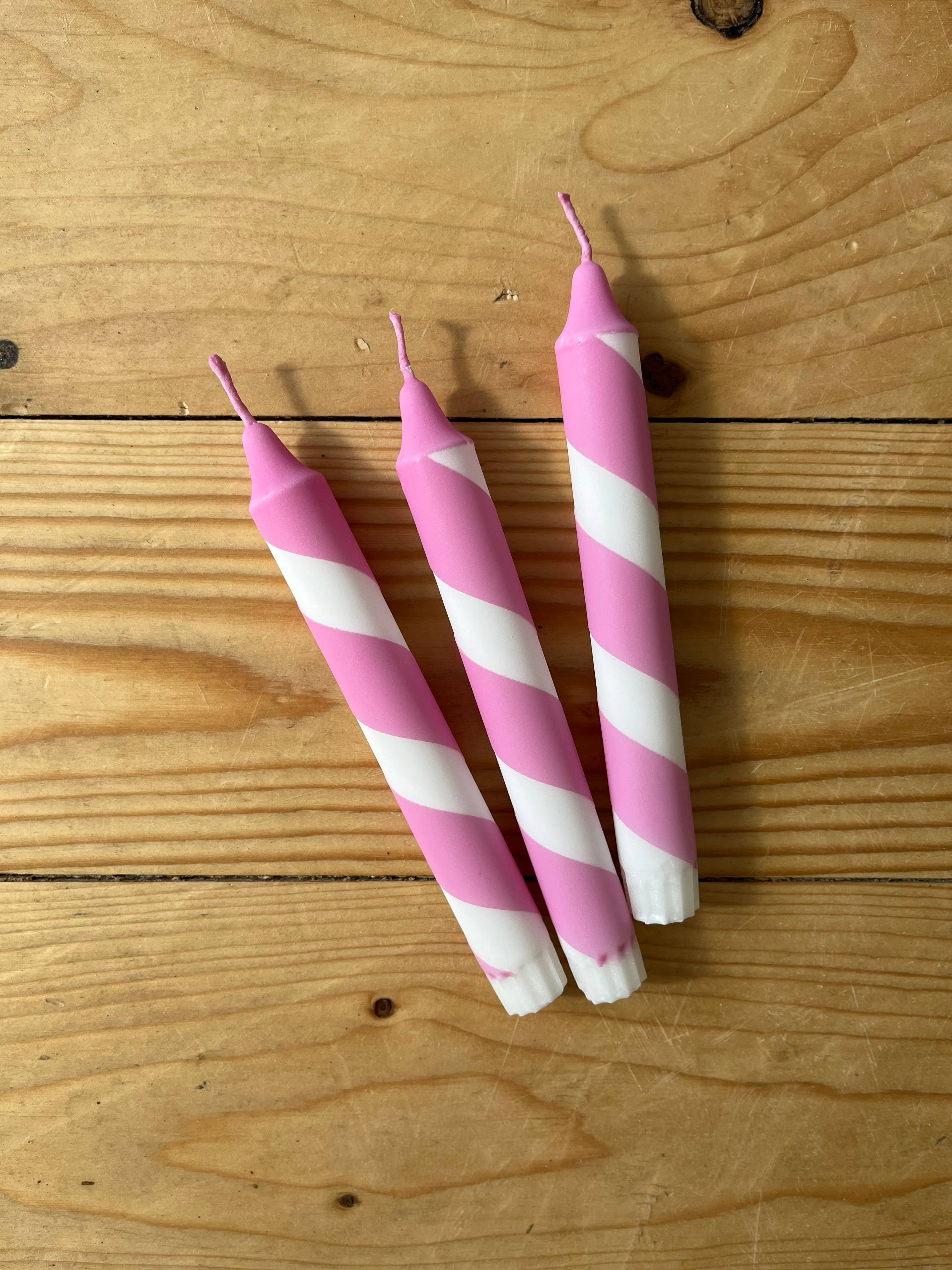 Three pink and white striped candles on a wooden surface