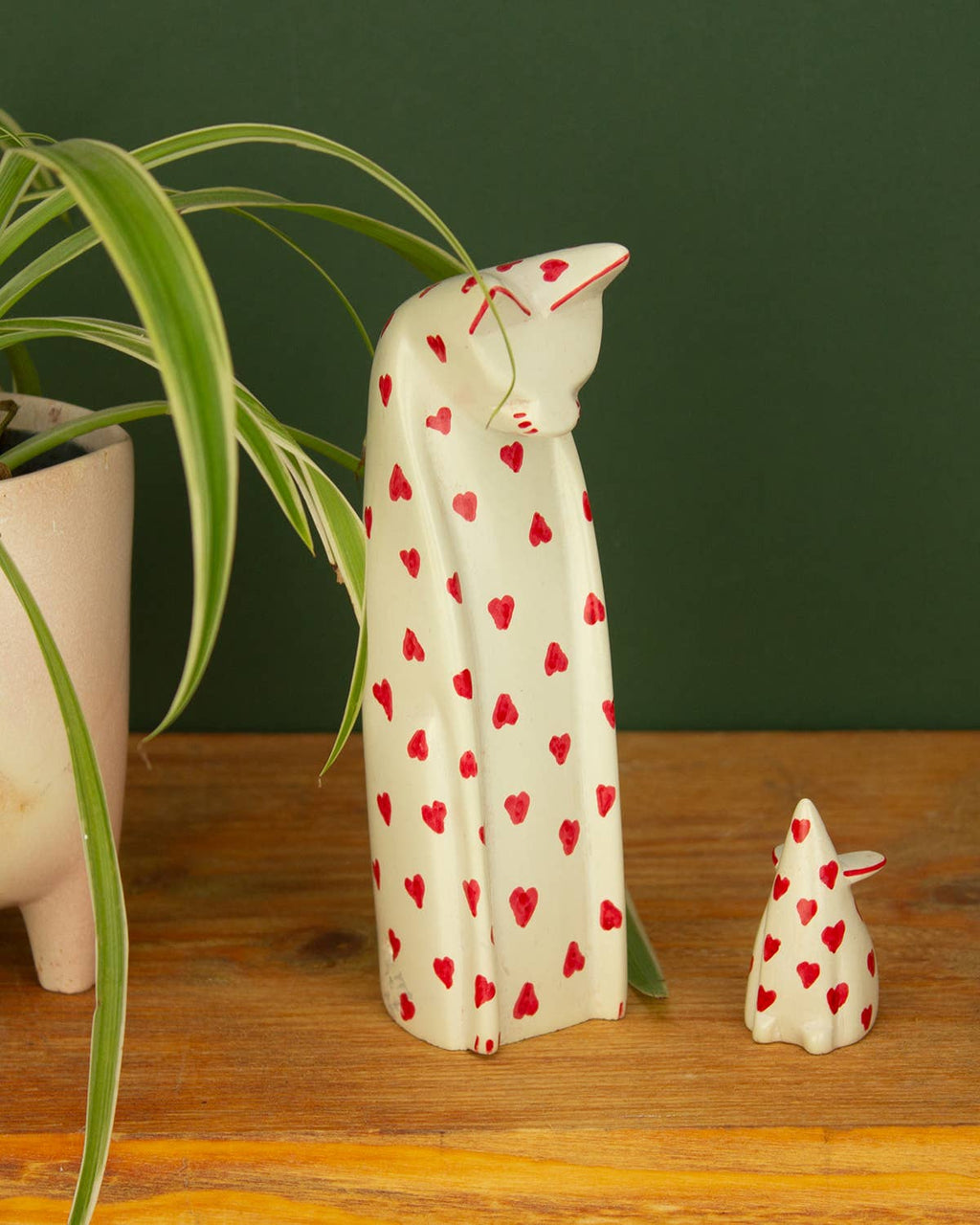 Soapstone cat and mouse figurines with red heart patterns on a wooden surface with a green plant in the background.