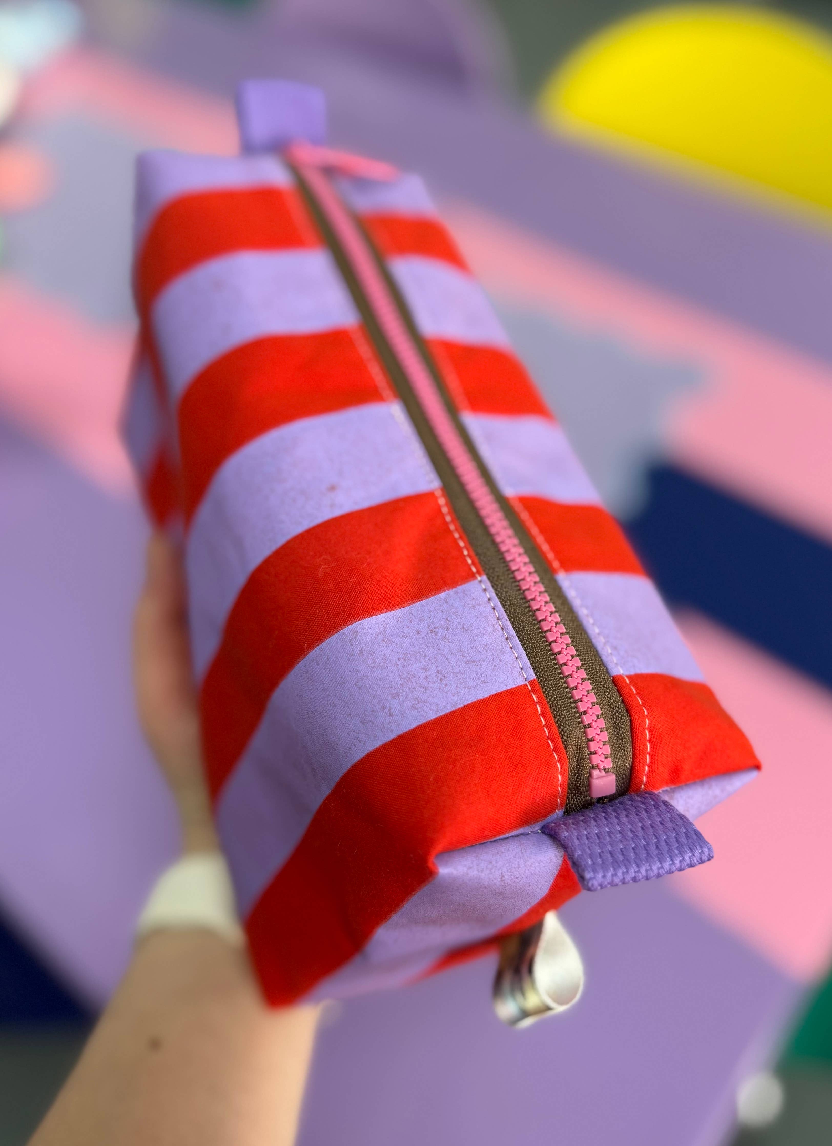 Red and white striped pouch with a zipper held by a hand against a colorful background