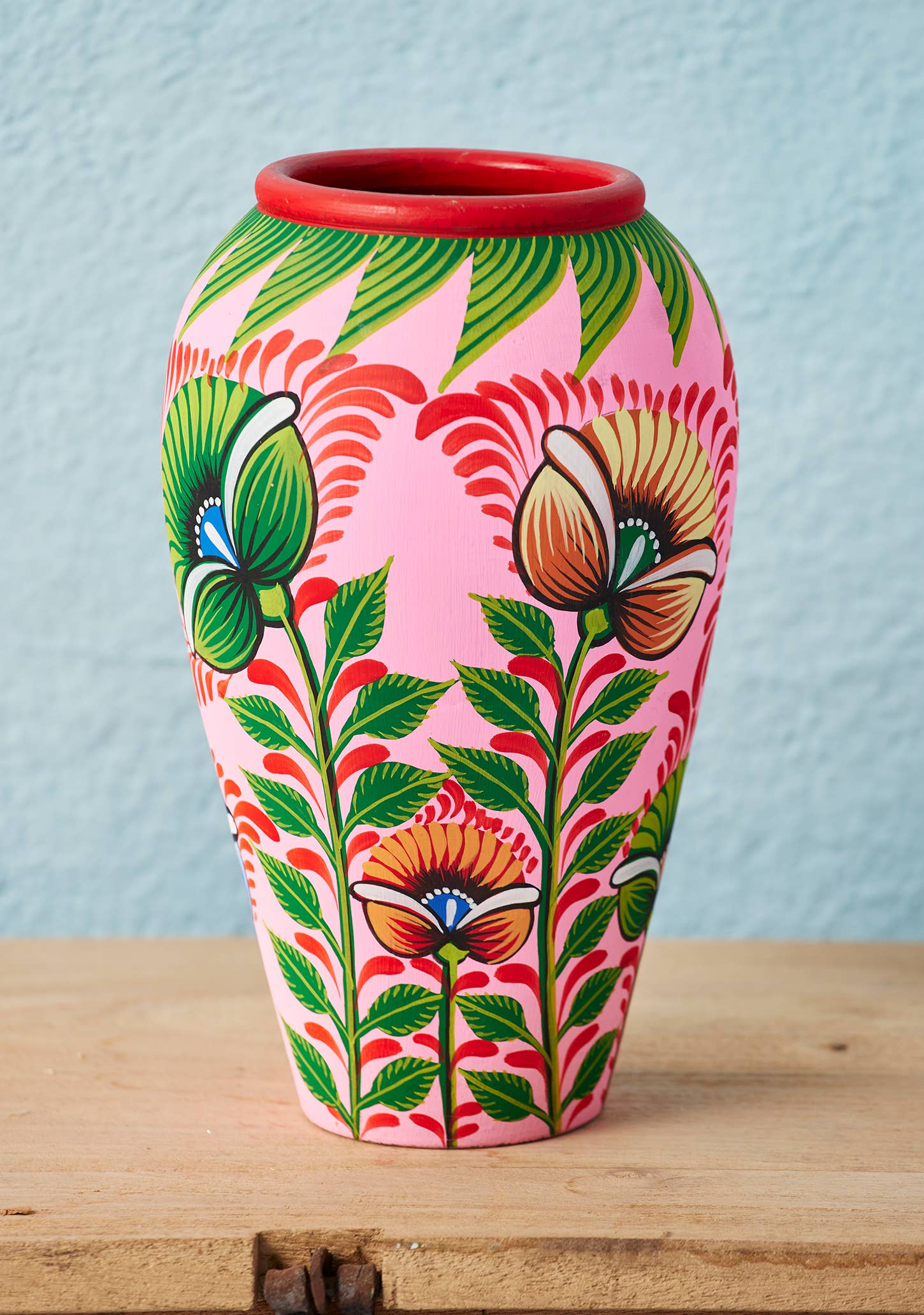 Colorful floral-patterned vase on a wooden surface with a light blue background