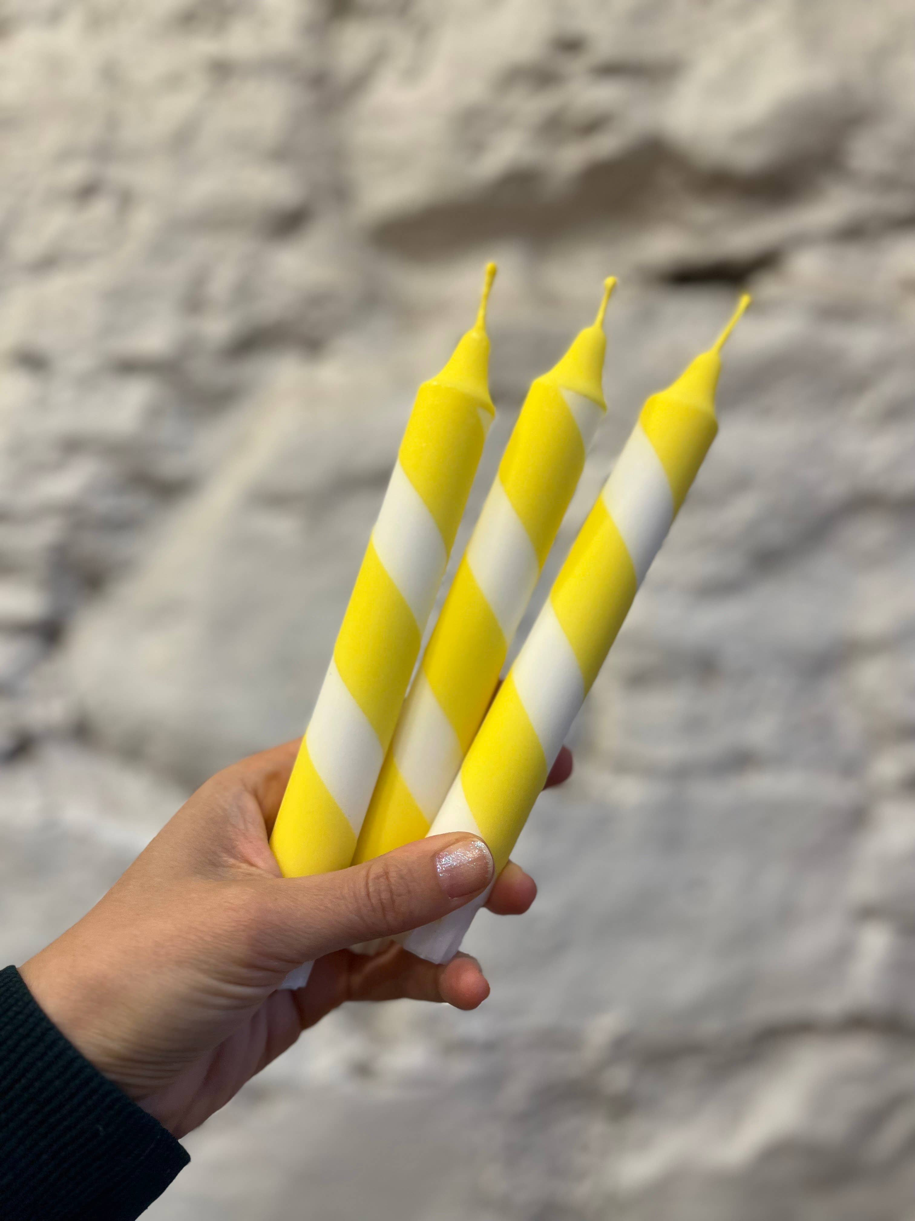 Hand holding three yellow and white striped candles against a stone wall background
