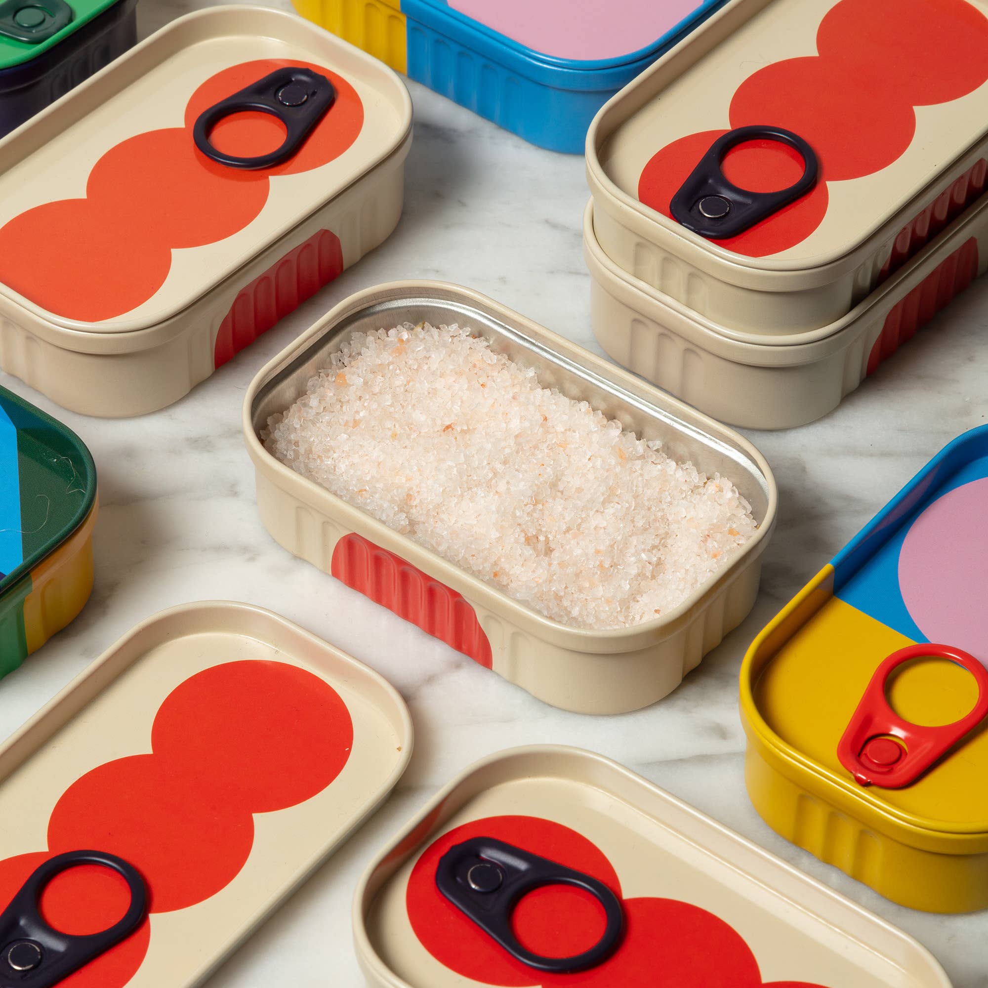 Colorful food containers with red circular designs on a light gray surface