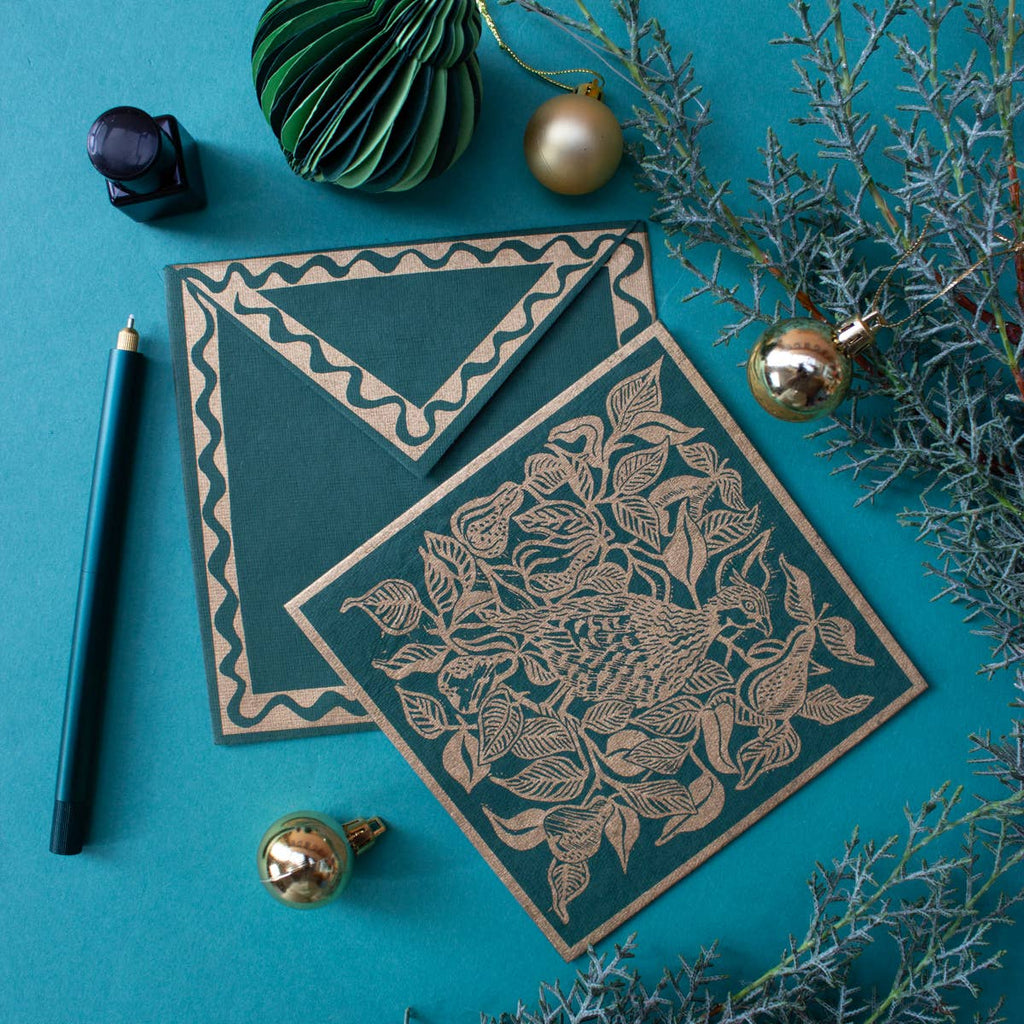 Decorative card with intricate design on a teal background with greenery and ornaments.