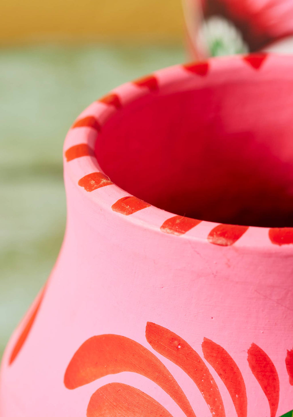 Close-up of a pink ceramic pot with orange floral patterns on a blurred green background