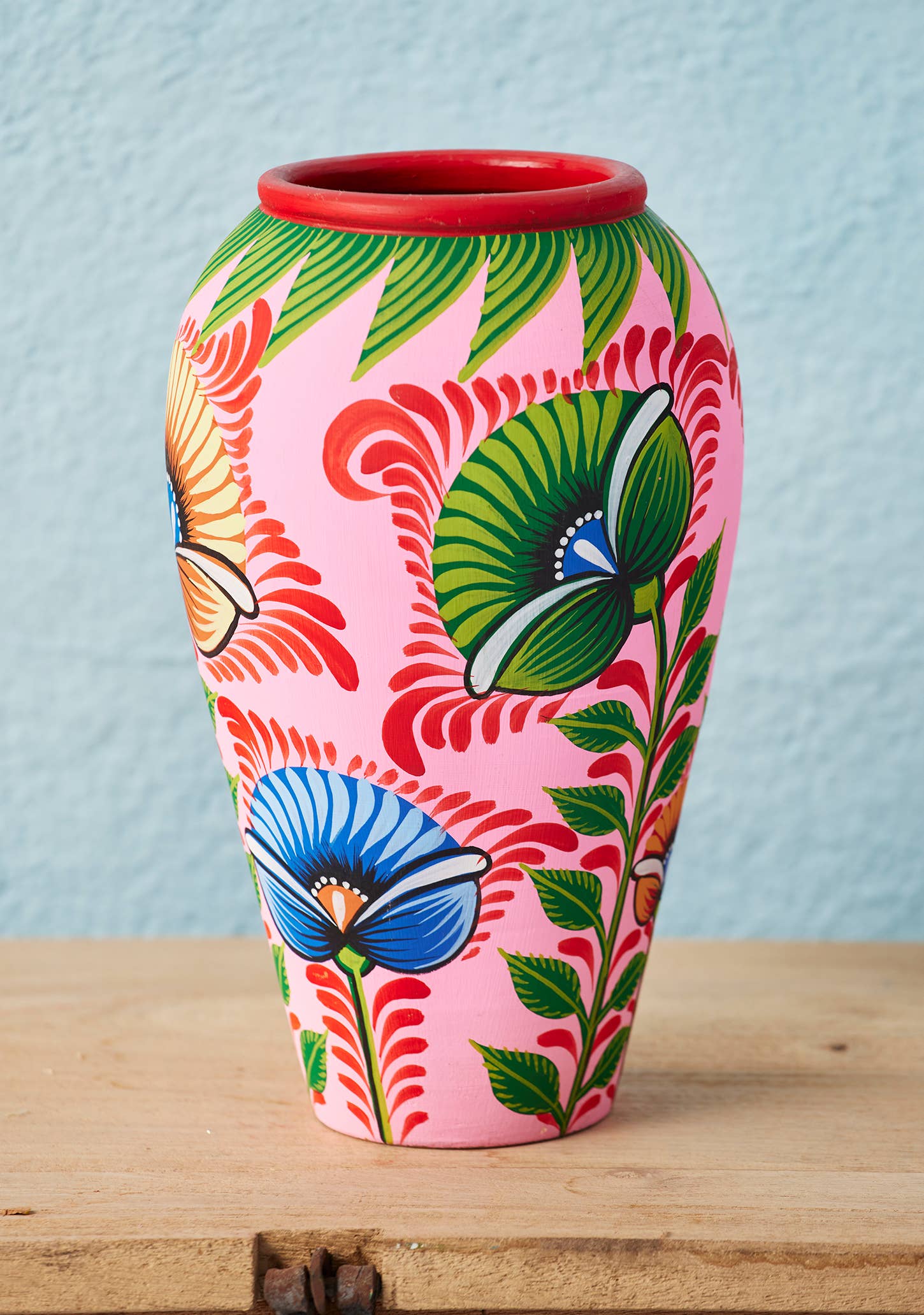 Colorful vase with butterfly and leaf design on a wooden surface and light blue background