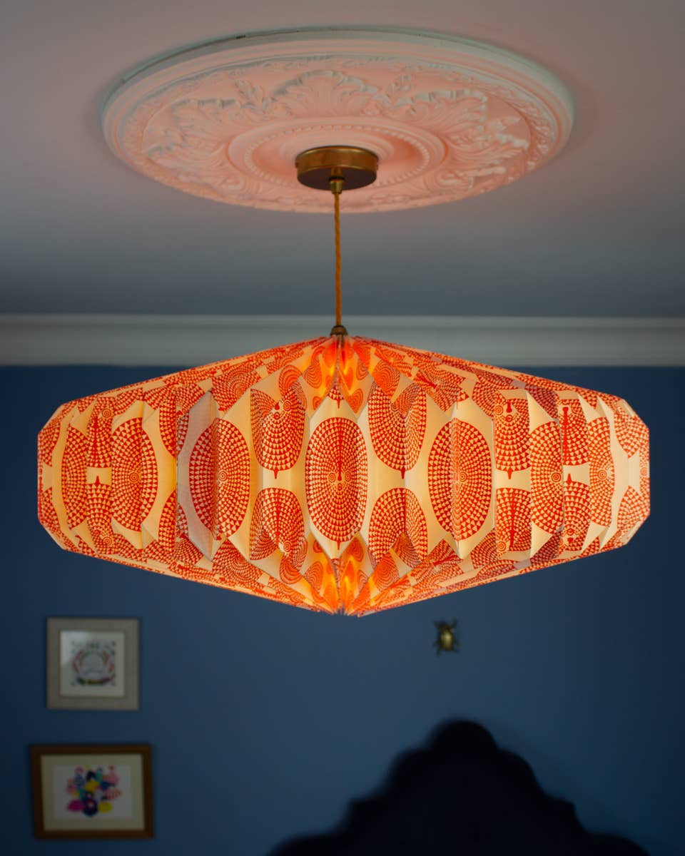 Decorative ceiling light fixture with orange patterned shade against a blue wall.
