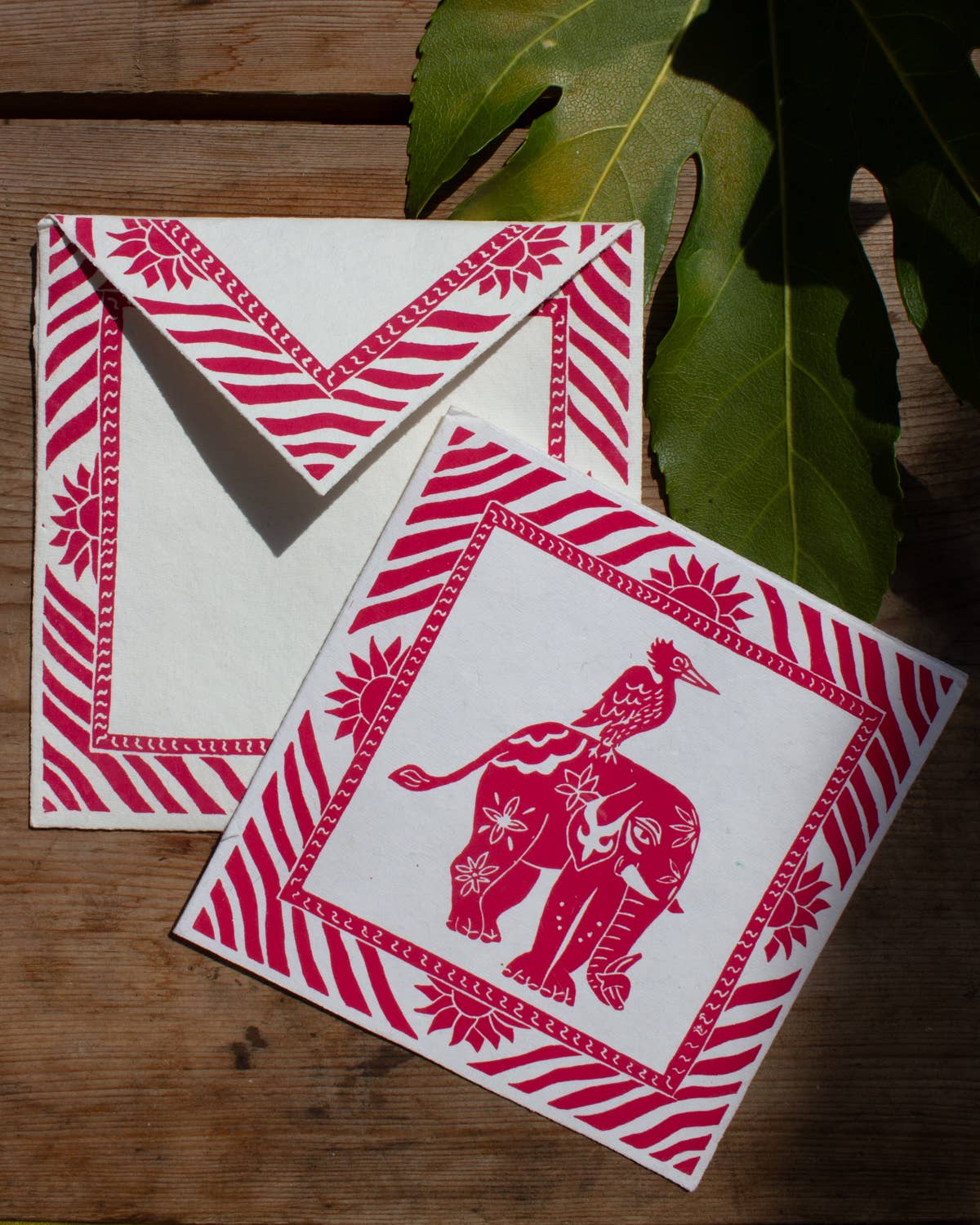 Two red and white patterned cards on a wooden surface with leaves in the background