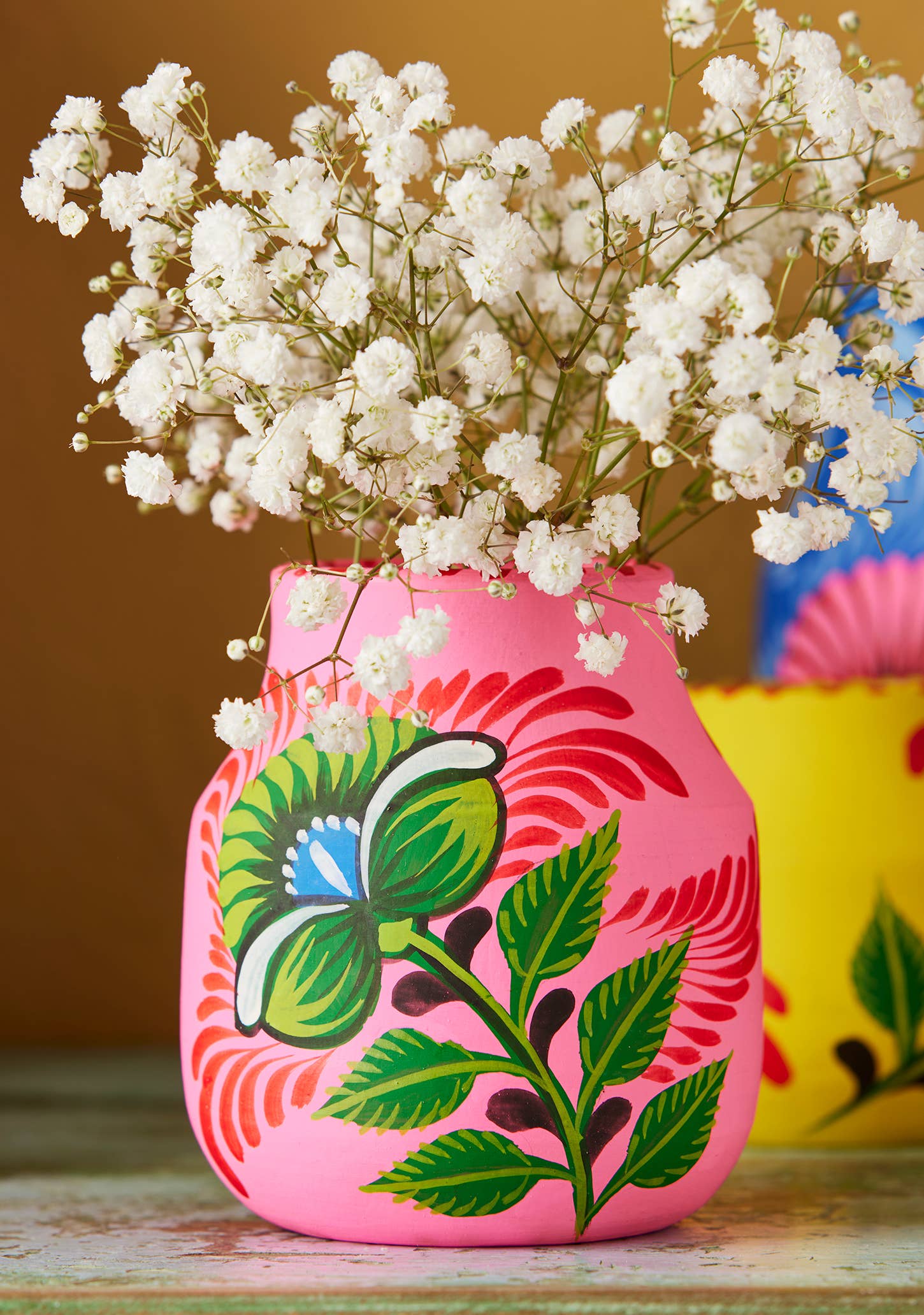 Decorative pink vase with floral design and white flowers on a wooden surface.