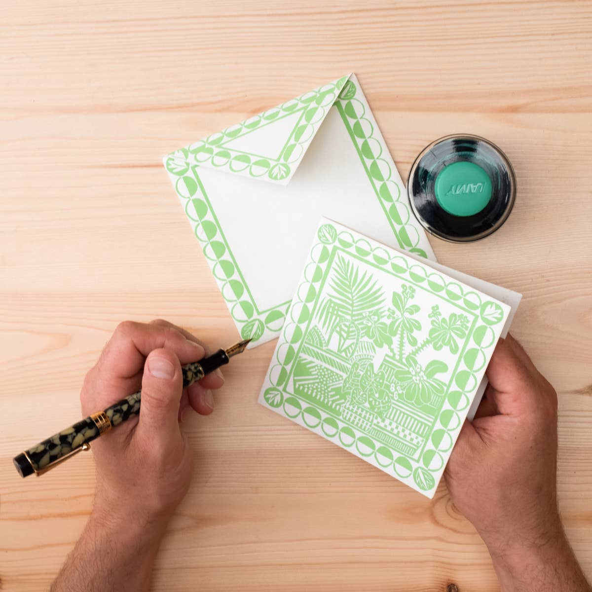 Person holding a pen and a stack of green patterned cards on a wooden surface.