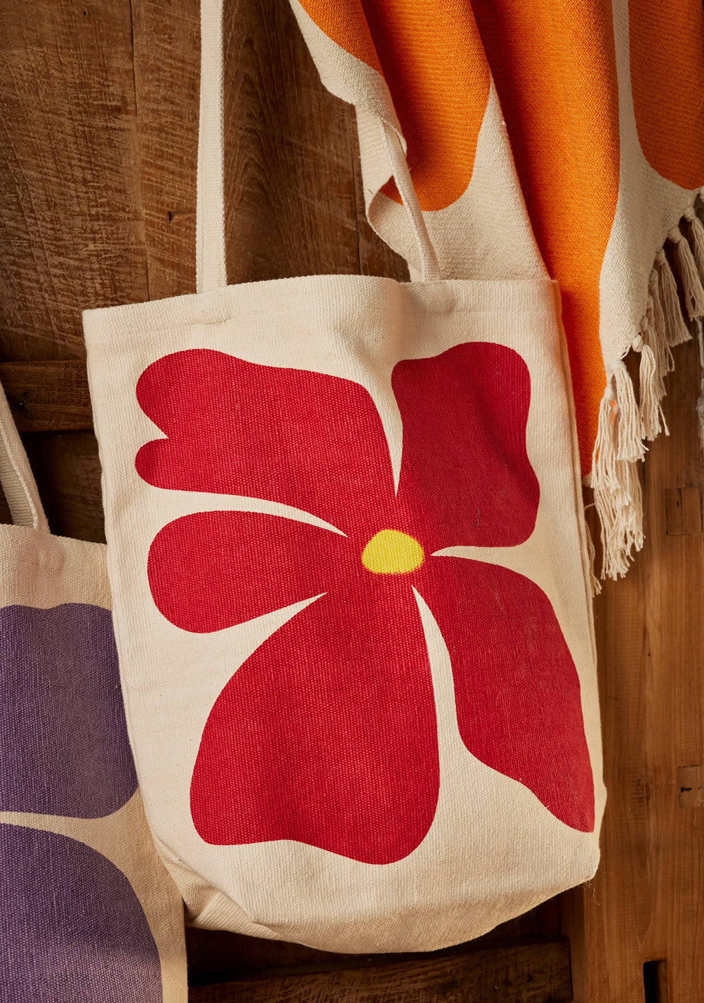Beige tote bag with a red flower design on a wooden surface