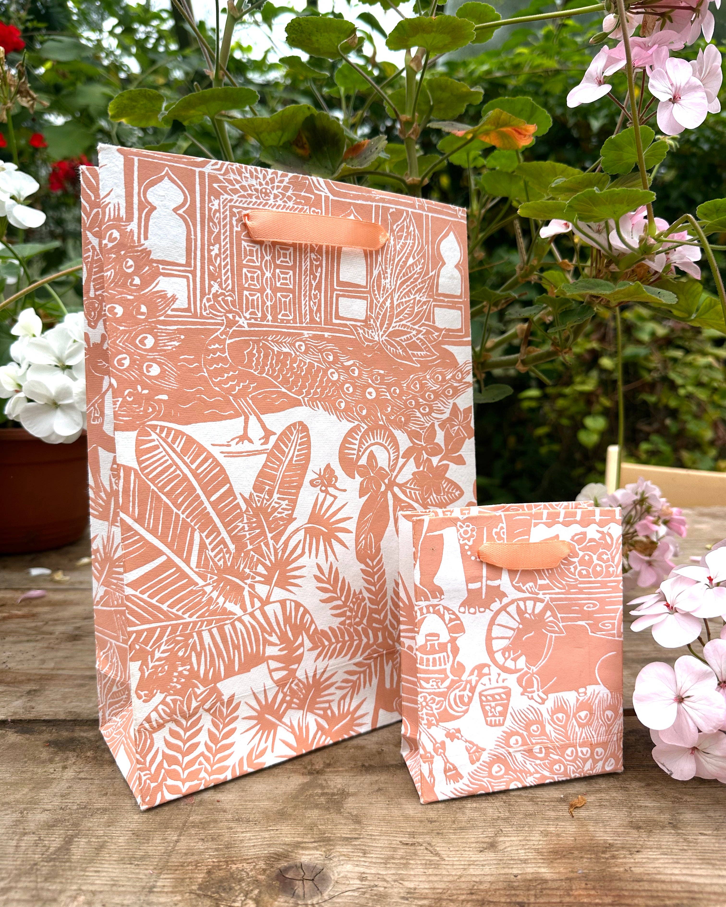 Two patterned paper bags on a wooden surface with flowers in the background