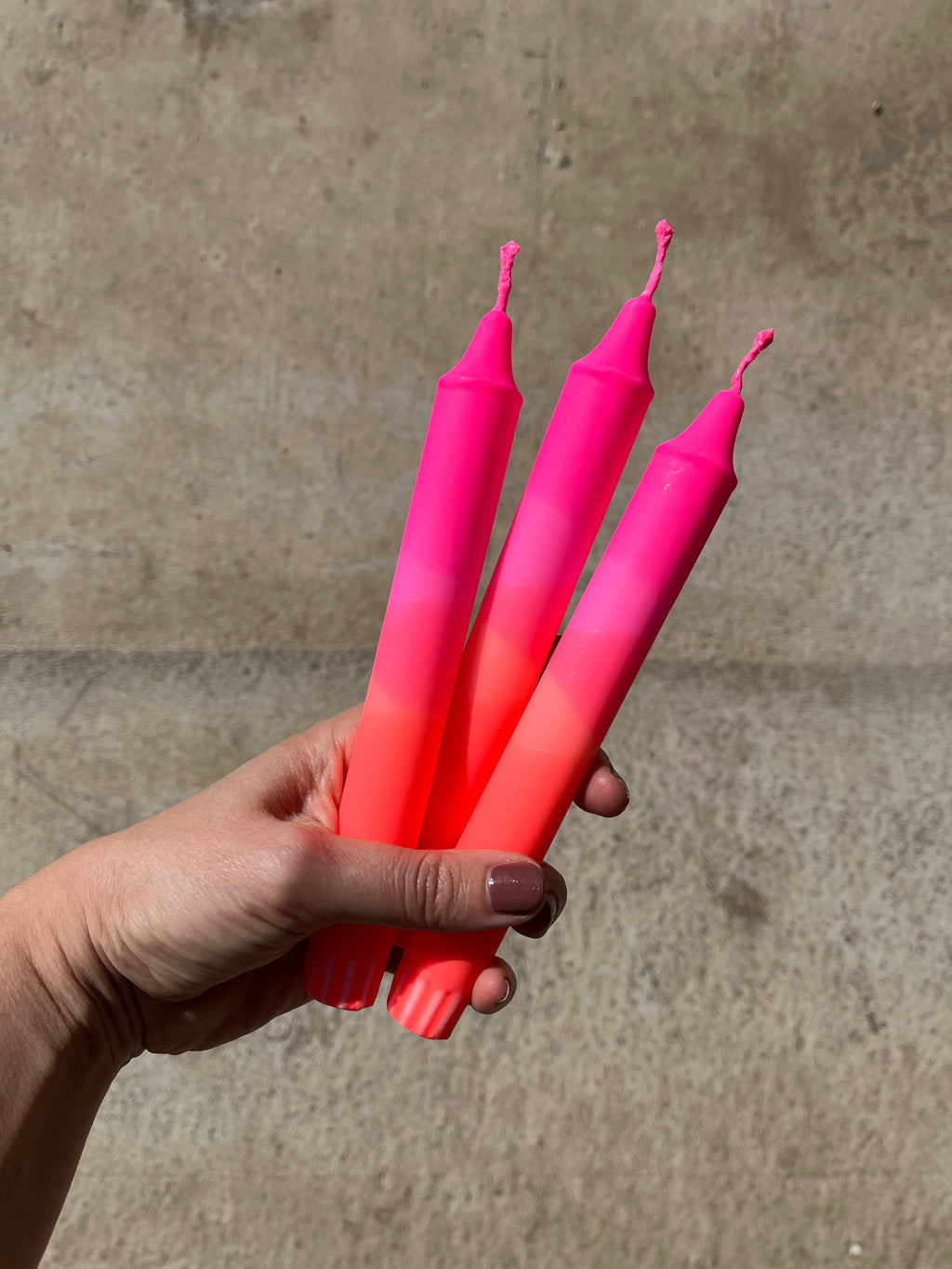 Hand holding three pink and red gradient candles against a concrete background